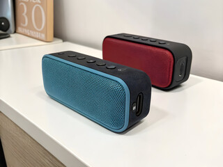 Obraz premium Teal and Red Portable Bluetooth Speakers on White Surface Close Up View Showing Speaker Grilles Buttons and Ports