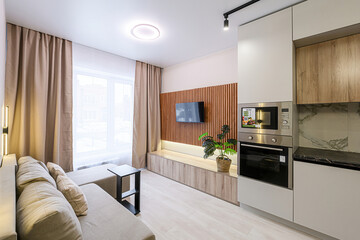 Cozy apartment interior with a sofa, TV, and modern kitchen. Neutral tones and natural light create a warm atmosphere