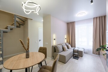modern living room with a sofa, table, chairs, and stairs. Neutral color palette with beige walls and light wood floors
