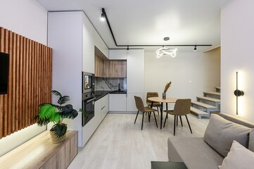 Fototapeta premium modern studio apartment with a kitchen, dining area, sofa, and stairs to a loft. Neutral color palette and minimalist design