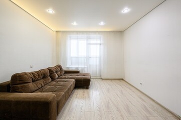 bright living room featuring a brown sectional sofa, light wood floors, a window with sheer curtains, and white walls illuminated by recessed lighting