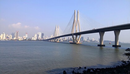 Fototapeta premium A long cable-stayed bridge stretches across calm water, a city skyline in the background under a clear sky