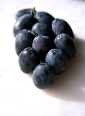 Close-up of fresh ripe plums on a light background. A delicious seasonal fruit perfect for jams, preserves, or as a sweet filling for rustic galettes and homemade desserts.