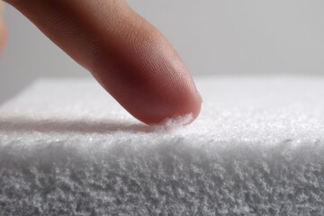 Fototapeta premium A person gently presses a fingertip against a soft white foam surface, showcasing its texture and softness in natural light Generative AI