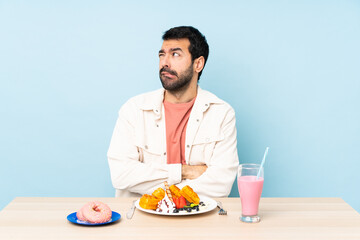Man at a table having breakfast waffles and a milkshake with confuse face expression