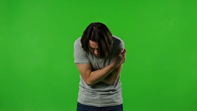 Man Shivering on Green Screen - A young man with long brown hair is shown shivering and hugging himself for warmth against a bright green screen background. He appears cold and uncomfortable.