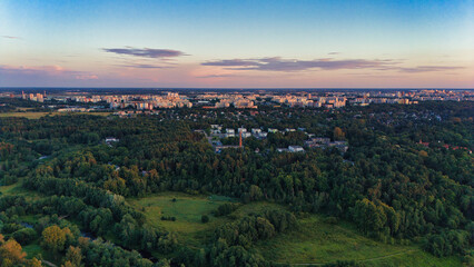 Fototapeta premium Aerial Panorama of City Skyline and Green Forest at Sunset