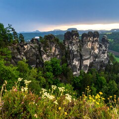 Scenic view of towering sandstone rock formations amidst lush greenery, wildflowers in the foreground, and a cloudy sky