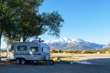 A trailer home park set under leafy trees, with a stunning backdrop of snowcapped mountains.