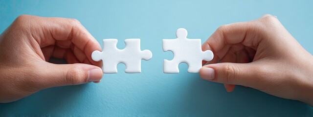 Two hands hold separate white puzzle pieces on a light blue surface