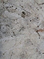 The image shows a close-up of a weathered, textured surface, likely concrete or stone, with cracks, dirt, and discoloration.

