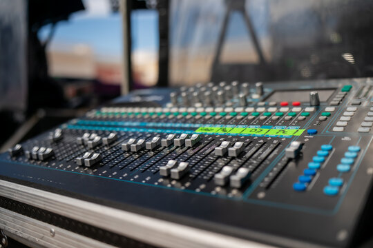 Professional audio mixing console with sliders, knobs, and illuminated buttons, outdoor stage sound engineering equipment used for live music event production and audio balancing