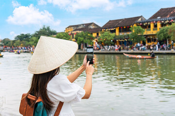 Happy Asian tourist woman wearing Non La (traditional Vietnamese hat) enjoy sightseeing in Hoi An city Vietnam