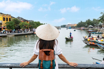 Happy Asian tourist woman wearing Non La (traditional Vietnamese hat) enjoy sightseeing in Hoi An city Vietnam