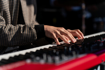 Piano keyboard in red color with musician hands performing live, stage performance detail with closeup view, music instrument, creative expression, artist fingers moving across keys in concert