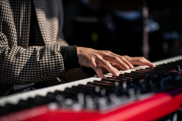 Pianist performing live with hands on modern stage keyboard, close-up of keys and fingers, red electronic piano detail symbolizing creativity, sound, art, melody, music performance and inspiration