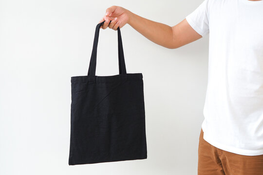 Young man hand holding black canvas tote bag on white background. Reusable eco bag for shopping. Eco friendly concept. Mockup for you designs.