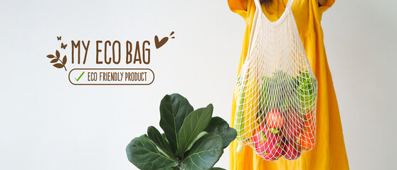 Woman holding mesh shopping bag with organic apple, corn, carrot, dragon fruit and lettuce on white background. Reusable shopping bag. Zero waste. Plastic free. Eco friendly concept.