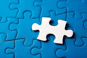 Obraz premium A single white jigsaw puzzle piece stands out against a vibrant blue background of assembled puzzle pieces symbolizing uniqueness and a missing element