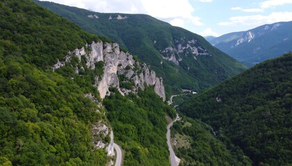 Naklejka premium Winding road through lush green mountains with steep, rocky cliffs