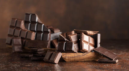 Broken bitter and milk chocolate bars on a brown background.
