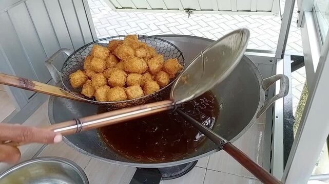 Street food vendor tahu crispy or frying tofu cubes in hot oil, scooping the golden brown pieces with a strainer from a large wok.
