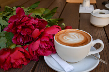 Romantic morning coffee with latte art and fresh red peonies on wooden table