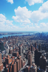 Fototapeta premium Aerial view of bustling cityscape with numerous skyscrapers under bright blue sky and scattered clouds, showcasing urban architecture and vibrant city life