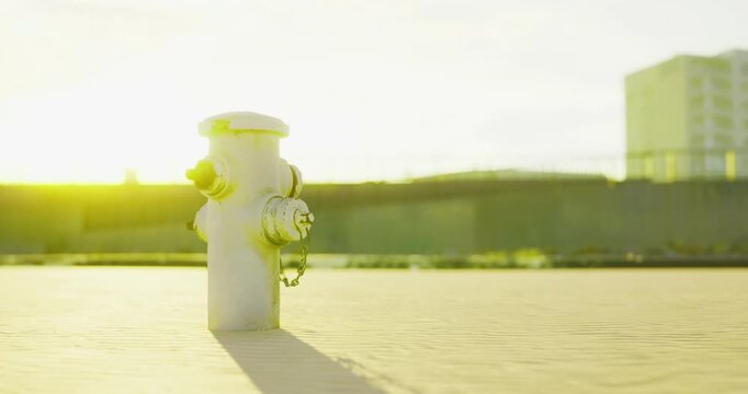 In a bright morning glow, a fire hydrant stands alone on a sandy surface near an urban construction site.