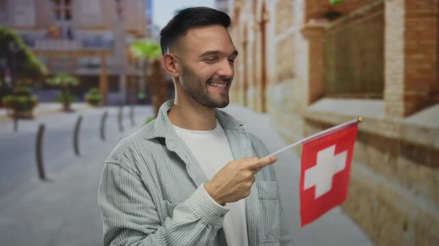 Young man smiling and holding a switzerland flag standing outdoors in an urban city street setting showcasing multicultural pride and diversity in a vibrant cityscape.