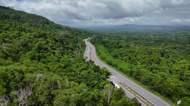 Drone footage of the aerial view of a winding road cutting through lush green forest. Scenic highway number 304 in Thailand links the Bangkok area to Nakhon Ratchasima in the northeastern region