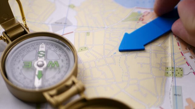 Hand holds brass compass above detailed map. Concept of military operation planning. Tactical decision point. Focus on terrain, coordinates, strategic movement across urban zones