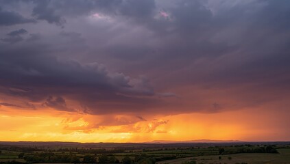 Fiery sunset over the countryside with dark, dramatic clouds and sun rays.