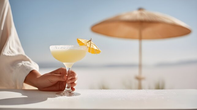 Hand holding margarita cocktail with lemon at beachside umbrella  