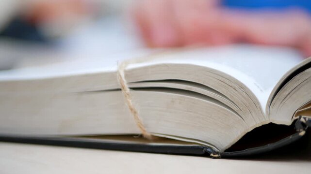 Hand keeps Bible open. Finger traces scripture. Wooden table holds sacred pages. Warm light enhances holy text. Ancient wisdom offers comfort. Faith connects with divine words