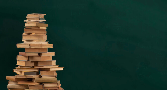 Stacks of books in the shape of pyramid or a mountain of textbooks against a background of a green school board.