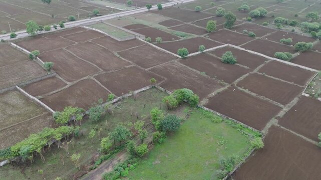 Aerial view of farmland with green patches,Drone shot of agricultural fields in rural area,Top view of empty farming plots with trees,Countryside farmland landscape with boundaries.


