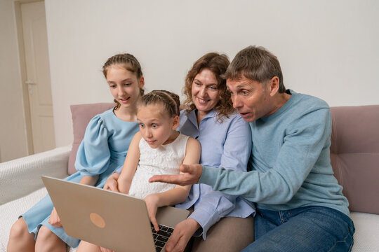 Family Laptop Home: Parents and daughters react, laughing while watching on a laptop together inside home.