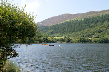 Mountain lake with boats, surrounded by lush green forest and rolling hills under a bright summer sky. Scenic outdoor landscape. High quality photo