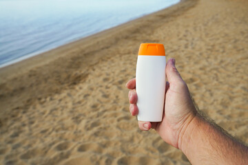 Hand holding sunscreen bottle on sandy beach by the sea