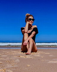 Young woman in black swimsuit sitting on sandy beach under clear blue sky in Australia