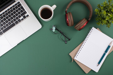 Flat lay workspace with laptop coffee cup headphones notebook glasses on green desk background copy space