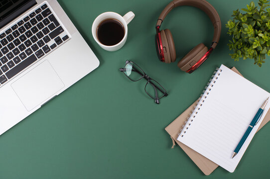 Flat lay workspace with laptop coffee cup headphones notebook glasses on green desk background copy space