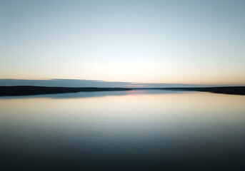 Fototapeta premium Tranquil Twilight Reflection: Calm Lake and Distant Forest Horizon