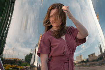 Woman in a rose dress poses beside giant reflective matryoshka sculptures with golden tops on Taras Shevchenko Embankment in Moscow