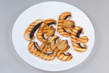 Grilled big button mushroom slices on plate on gray background