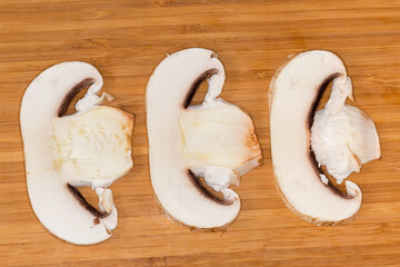 Slices of raw button mushroom on cutting board, top view