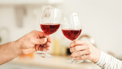 Holiday greetings, date at home and romantic evening. Domestic life and anniversary. Adult european man and female clink glasses with red wine in minimalist kitchen interior, empty space, cropped