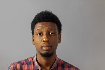 Obraz premium portrait of a young African man with neutral expression against a clean studio backdrop, ideal for illustrating diverse concepts and narratives.