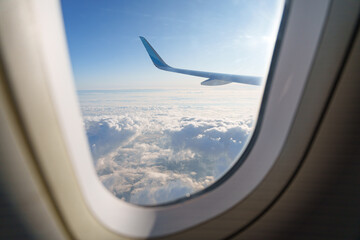 Fototapeta premium Airplane wing view above clouds with bright sunlight in the sky